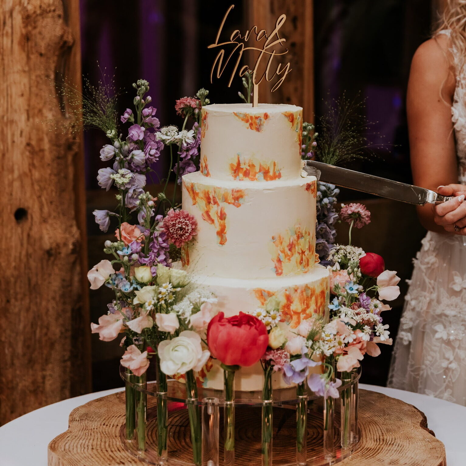 Swiss meringue buttercream encasing a three tier wedding cake to create a smooth, classic finish with flecks of bright pastel colour from orange, yellow and blue