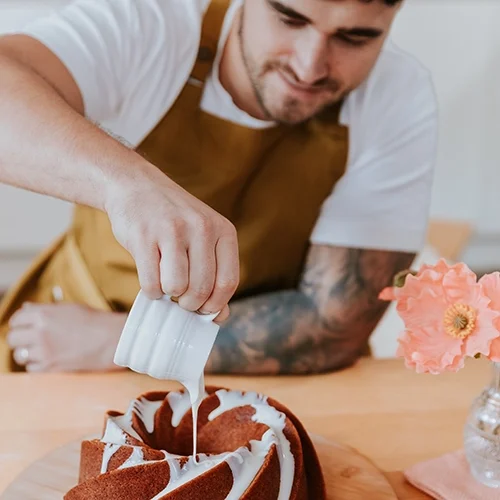 Matty pouring white icing onto an orange bundt cake