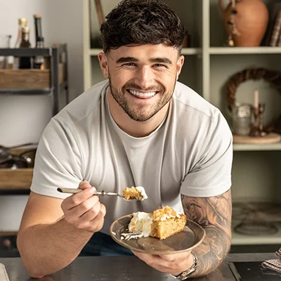 Matty holding a plate with cake and cream with a fork full of cake waiting to be eaten whilst smiling towards the camera