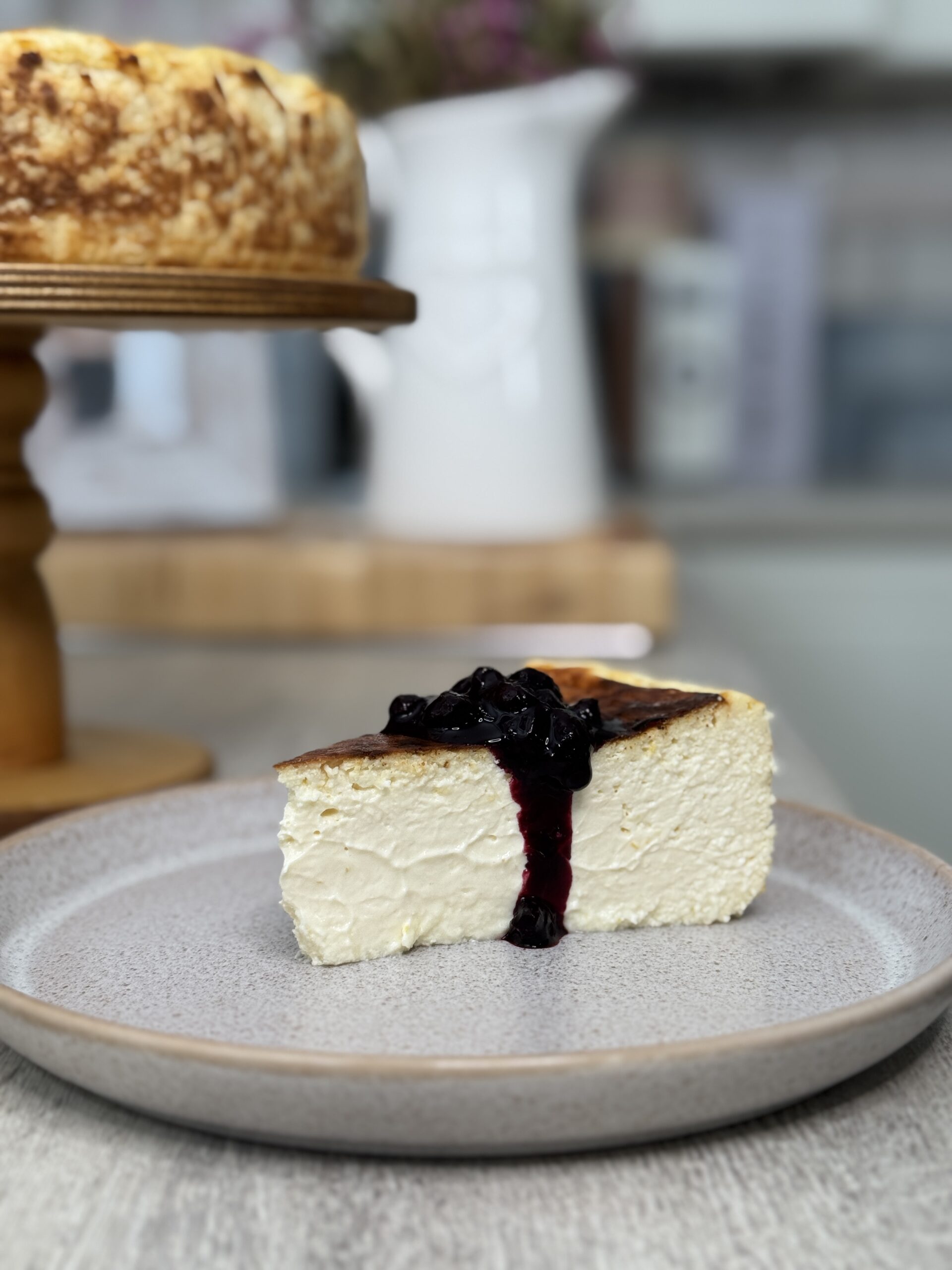 A slice of lemon basque topped with blueberry compote dropping down the side